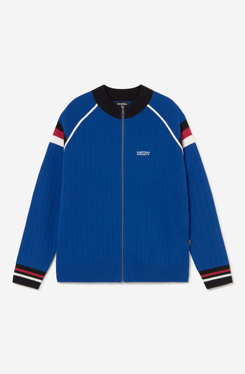Chaqueta de punto azul con cremallera, cuello bomber y detalles deportivos en blanco, negro y rojo.
