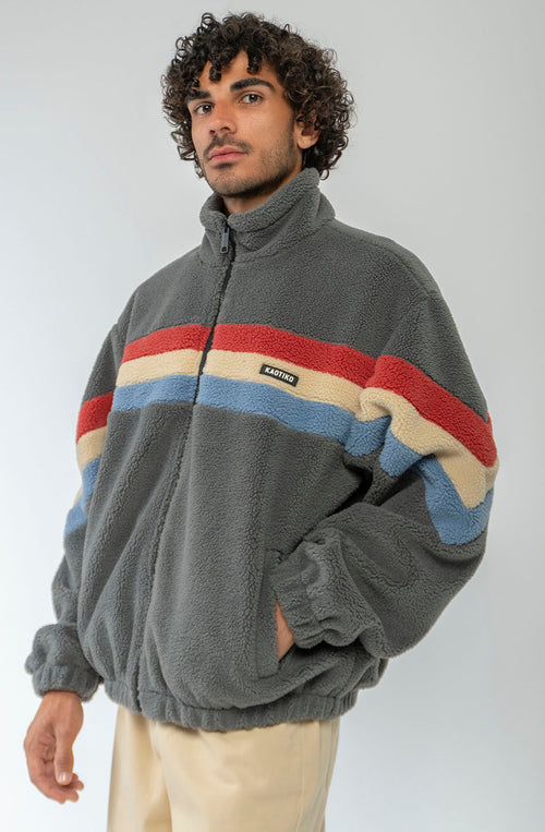 Polar Wabi Sabi Khaki de fleece con franjas rojas, beige y azules, cuello alto y cierre de cremallera.