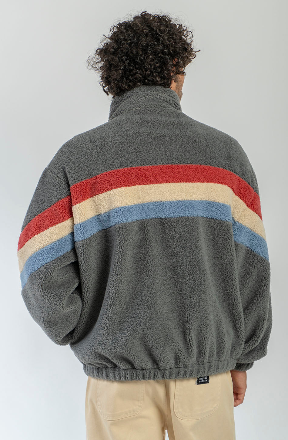 Polar Wabi Sabi Khaki de fleece con franjas rojas, beige y azules, cuello alto y cierre de cremallera.